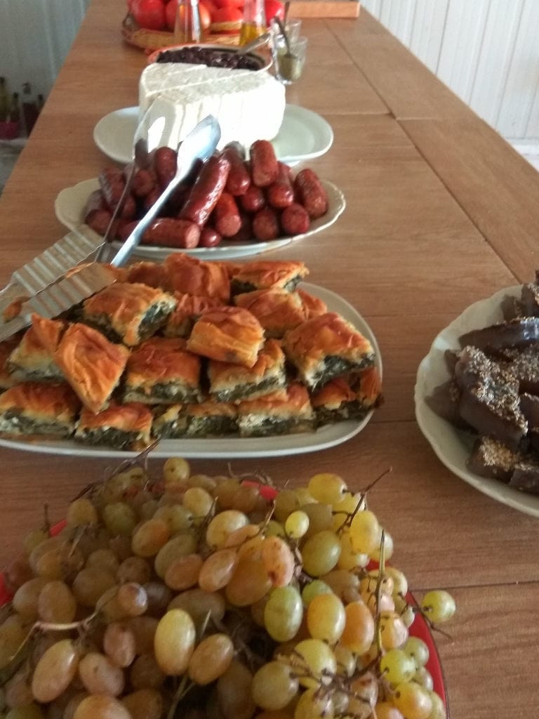 plates with white grapes, pie, meeat sausages, cheese on the wood table at Bio Goupios